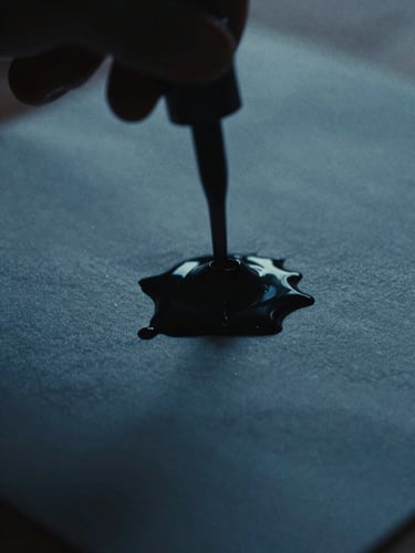 Moody close-up of ink pooling on textured paper, low-key dramatic chiaroscuro lighting, deep shadows and cool blue tones, 35mm film grain