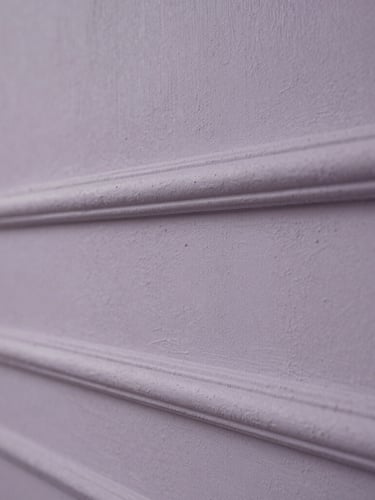 Macro photograph of hand-applied plaster texture, desaturated lavender-gray tones, soft side lighting, classical estate wall detail.
