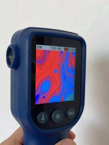 Close-up of a handheld thermal imaging camera screen displaying bright red and blue moisture mapping patterns on a plaster wall, sharp focus, crisp work lights, 35mm