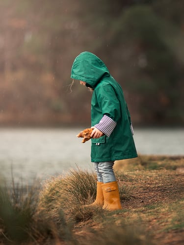 a little girl in a green raincoat and boots
