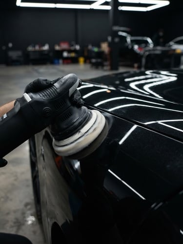 Sleek automotive photography of a dual-action polisher correcting a deep metallic black car panel, dramatic high-contrast workshop LED light lines reflecting off the paint, sharp macro focus, 35mm lens.