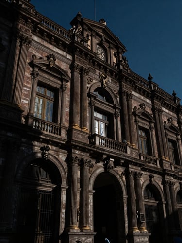 Low-angle heroic shot of an imposing CDMX court facade, dramatic chiaroscuro lighting, deep navy tones, sharp shadows on marble