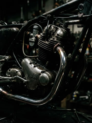 Dramatic low-key lighting close-up of a pristine motorcycle engine block and chrome exhaust pipes, high contrast, dark metallic textures, 35mm lens