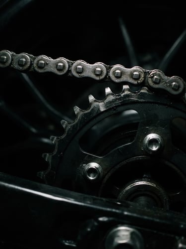 Close-up of a high-performance motorcycle chain and sprocket, metallic textures, dramatic low-key lighting, high contrast, 35mm lens