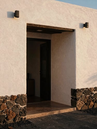 Architectural detail of a minimalist Canarian villa entryway, warm natural light casting soft shadows on textured stone walls, 35mm film aesthetic
