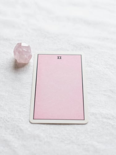 A single minimalist tarot card resting on a clean white linen surface next to a small pink quartz crystal, soft morning light, ethereal aesthetic