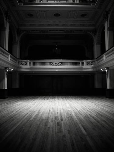 Symmetrical architectural shot of a grand New York ballroom, high-contrast black and white, dramatic empty space, crisp spotlight highlights, 35mm film.