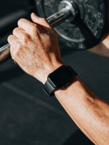 Close-up of a modern fitness wearable on an athlete's wrist during a heavy lift, high-contrast natural light, deep shadows, rich desaturated tones, 35mm