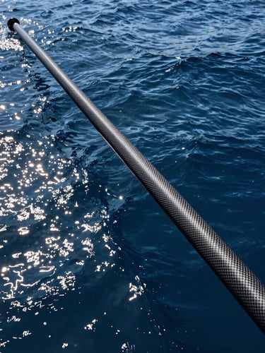 Wide-angle action shot of a heavy carbon rod bent to its absolute limit against a deep oceanic blue background, high-contrast midday sun reflecting off the water.