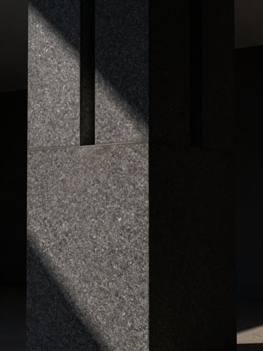 Abstract architectural crop, monolithic raw dark stone column, dramatic single-source chiaroscuro light, deep shadows, minimalist composition.