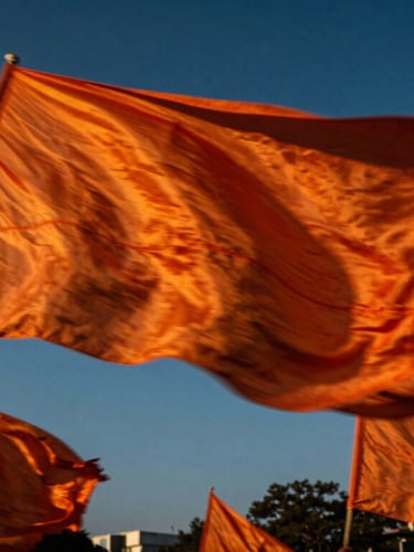 Dynamic low-angle shot of a massive saffron flag swirling against a deep blue sky during a street procession, motion blur, dramatic lighting.
