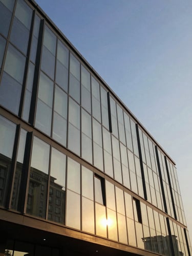 Crisp architectural geometry of DLF The Camellias glass facade reflecting golden hour light against a clear blue sky in Gurugram.