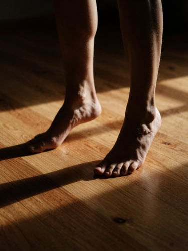 Dynamic low-key photo of feet mid-pivot on a warm wooden studio floor, dramatic side-lighting casting long shadows, rich contrast, subtle motion blur.