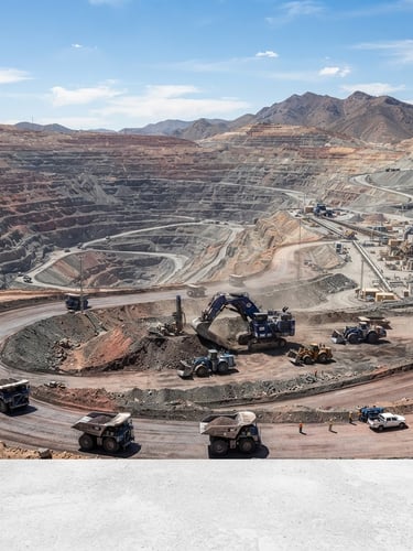 Wide panoramic shot of a modern, active open-pit mine site at daylight, with heavy machinery in the mid-ground and a clear blue sky, crisp industrial photography, sharp focus, safety-blue and charcoal tones.