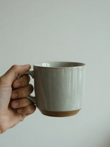 A quiet solitary moment of calm, a hand holding a warm ceramic mug in soft diffused overcast daylight, muted sage tones, shallow depth of field, 35mm photography