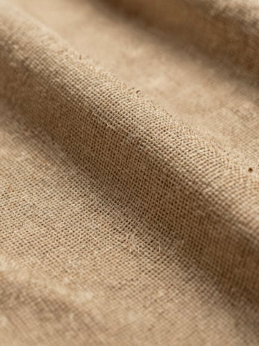 Macro photograph of a heavy-weave Belgian linen, warm sand color, dramatic side light emphasizing the thick natural slub and structural texture