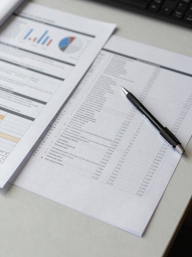 Close overhead shot of a research analyst's desk, printed statistical output and annotated survey instruments spread across a light-grey surface, a mechanical pencil resting on margin notes, soft diffused office light, no people visible