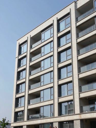 Wide elevation study of a completed multi-storey commercial building facade, finished stonework and glass curtain wall under clear midday light, right-hand framing with open sky to the left, no people