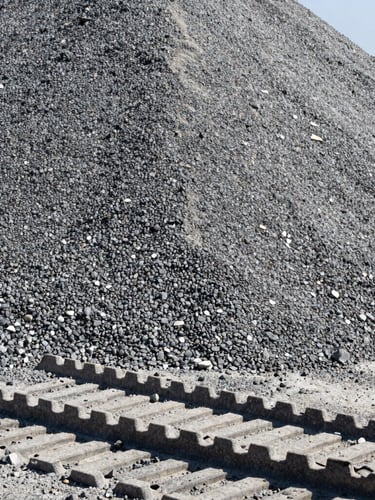 Close-up of raw gray gravel aggregates piled in a massive mound under direct sunlight, sharp focus on stone textures, heavy machinery tire tracks in the foreground, 35mm lens