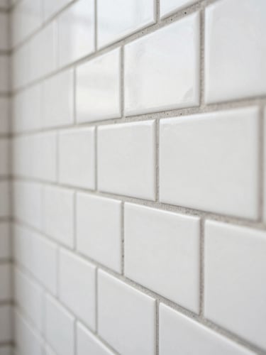 Macro close-up shot of perfectly aligned white subway tiles with clean grey joints, natural daylight from the side, highlighting precise craftsmanship and technical execution.