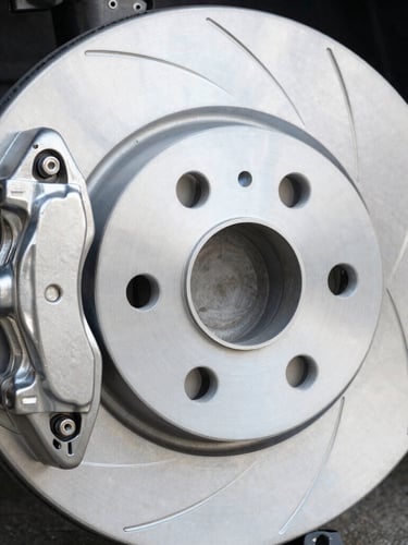 Macro shot of a pristine metallic brake disc and brake caliper, cool daylight reflecting off the clean steel surface, professional industrial photography, 50mm lens