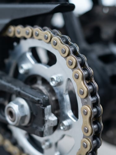 Close-up of a pristine metal motorcycle drive chain and rear sprocket, bright cool daylight, sharp metallic details, clean industrial photography, 50mm lens