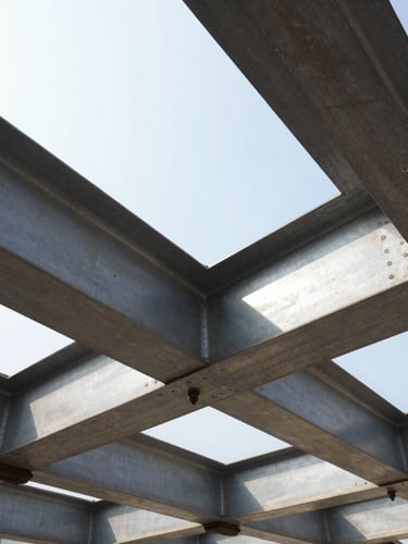 Low-angle heroic shot of massive steel structural beams being bolted together on an active industrial construction site, high-contrast morning sunlight, grit and dust