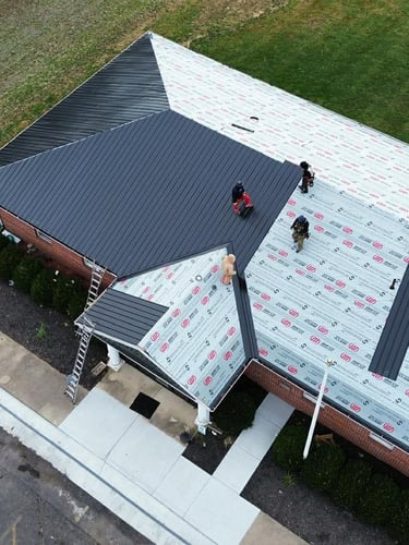 Aerial view of contractors installing a new black metal roof on a residential home with protective underlayment.