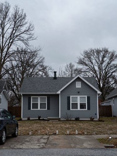 Overcast exterior of a small house, a car in the driveway, bare winter trees, flat digital gray, no filters
