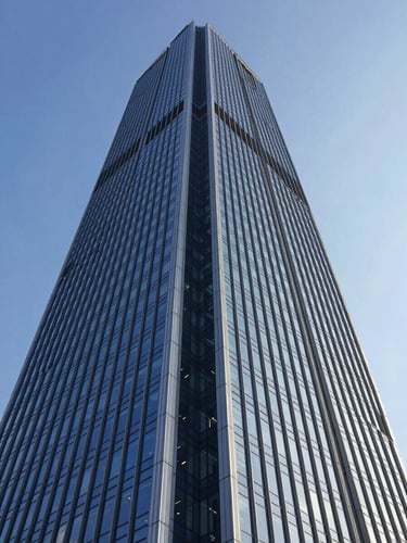 Wide-angle low-perspective shot of a towering modern skyscraper with a deep blue glass facade reflecting cool daylight, sharp structural lines, architectural photography