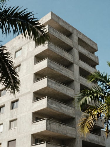 Candid medium shot of a modern concrete apartment building in Dakar under bright Sahelian sunlight, green palm leaves framing the side, clean composition.