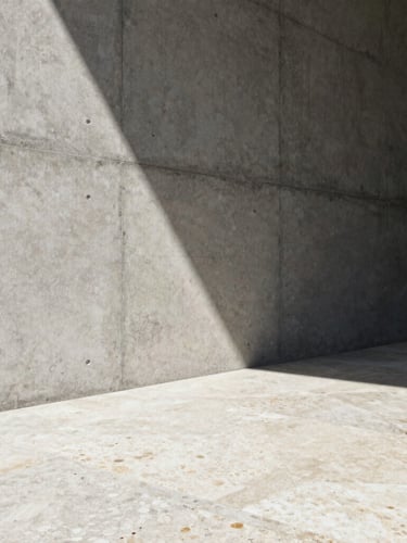 One-point perspective elevation of a raw concrete wall meeting a travertine floor, high-contrast natural sunlight creating a sharp diagonal shadow