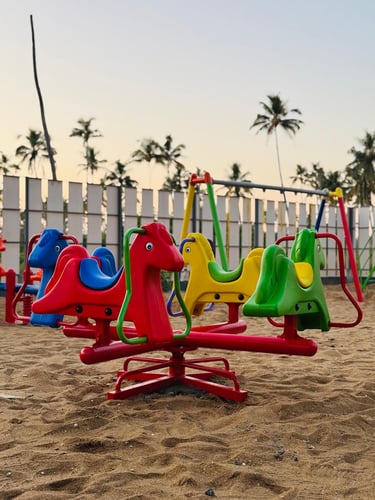 Colorful horse-shaped roundabout on a sandy playground with palm trees in the background.