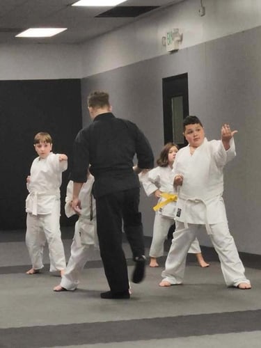 Children in white karate gi practice martial arts strikes during a youth training class.