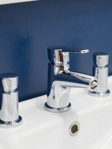 Sharp close-up of clean chrome bathroom fittings, bright daylight reflecting off metallic surfaces, 35mm lens, clean navy background