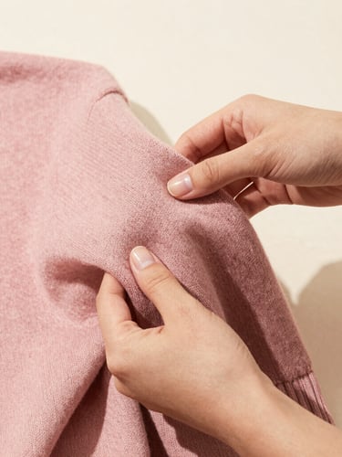 Close-up of hands gently folding a soft chocolate pink cotton knit sweater, bright editorial fashion photography, natural daylight
