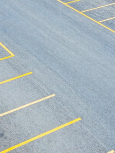 Overhead aerial view of an organized surface parking lot with clean yellow painted lines, sharp geometric layout, high contrast, bright daylight.