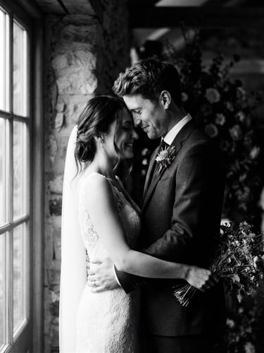 High-contrast black and white wedding portrait, a quiet moment between a couple under dramatic window light, editorial 35mm film look, rich shadows