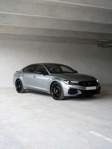 Wide shot of a late-model European sedan on clean white cement in a parking structure, three-quarter front angle, neutral studio-style daylight, no reflections, vehicle fully visible, generous negative space to the left