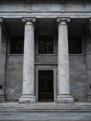 Symmetrical architectural perspective of a neoclassical financial institution facade with clean stone pillars, cool overcast daylight, desaturated navy and slate tones, 35mm