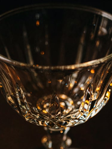 Extreme macro close-up of a heavy-bottomed geometric crystal glass rim, single-source golden amber directional light catching sharp facets, pitch black background, 35mm film style