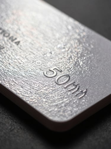 Sharp macro photography of a heavy cardstock business card with glossy spot-UV coating reflecting bright studio light, shallow depth of field, 50mm, dark paper texture.