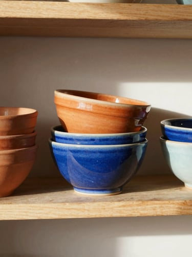 Warm sun-drenched kitchen shelf with stacked terracotta and cobalt blue ceramic bowls, soft shadows, 35mm