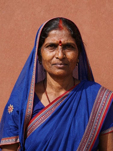 Dignified eye-level environmental portrait of a rural Indian woman leader looking directly at the camera, harsh authentic midday sun, warm terracotta tones, 35mm lens.