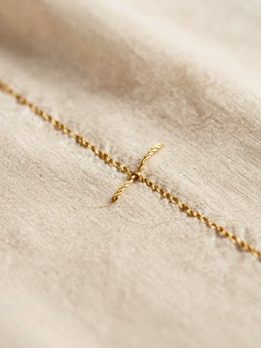 Macro shot of delicate gold embroidery thread on soft organic champagne cotton fabric, warm natural daylight, shallow depth of field, 35mm