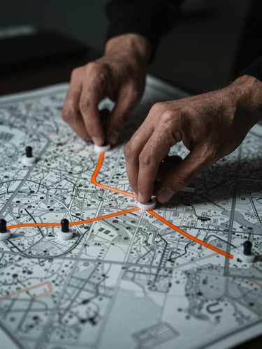 Dramatic close-up of hands moving physical markers across a tactical tabletop map, low-key side lighting, desaturated cool tones, sharp orange accent line.