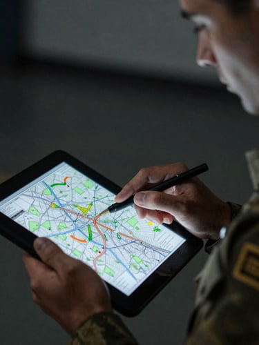 Close-up of a military officer in uniform analyzing a tactical map on a tablet screen, low-key dramatic side lighting, cool desaturated tones with sharp orange accents.