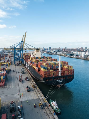Wide-angle environmental shot of a massive container ship docked at a deep-water port, cool blue tones, bright daylight, sharp focus, 35mm