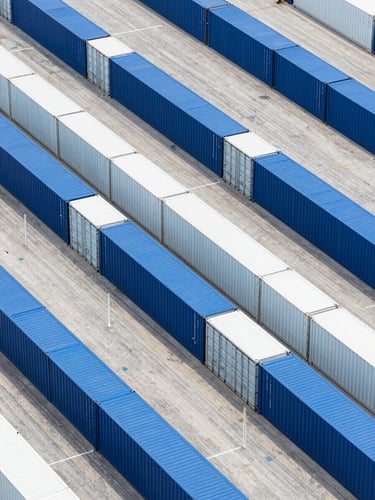 Overhead geometric shot of perfectly aligned blue and white shipping containers in a clean, modern dry port terminal, bright daylight