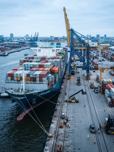 Wide-angle environmental shot of a massive container ship docked at a deep-water port, cool-toned daylight, sharp focus, 35mm